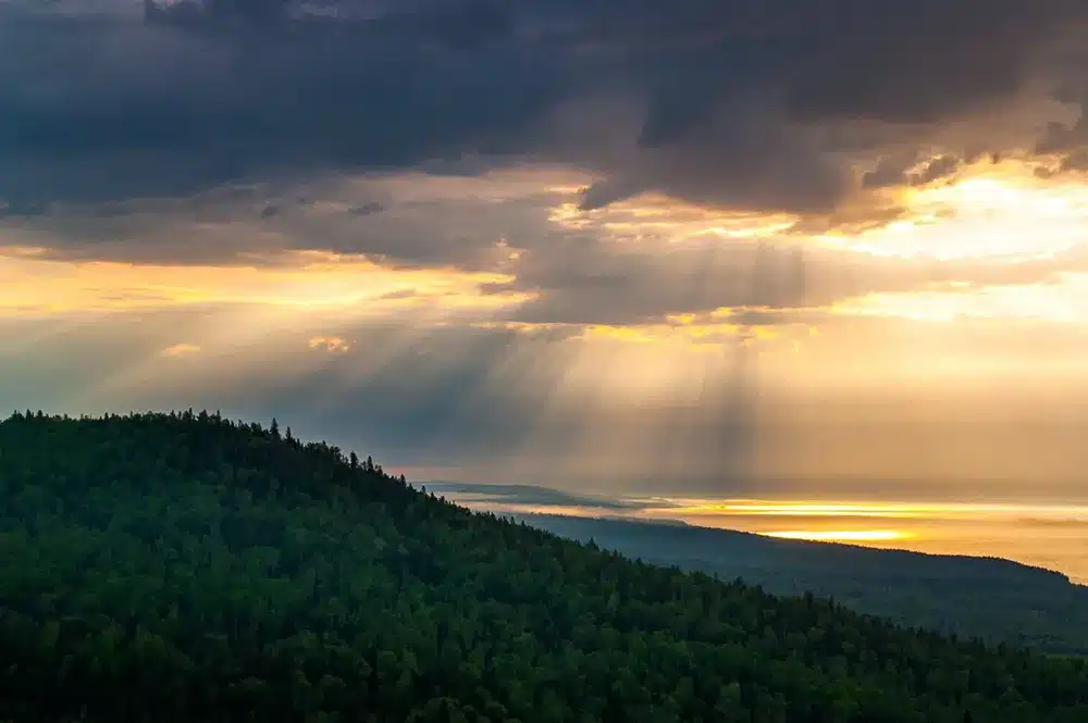 view of a sun peeking through storm clouds overlooking a forest
