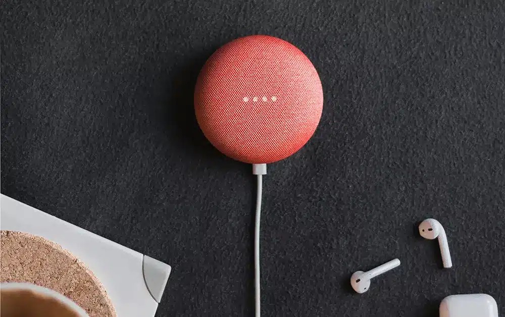 a google nest smart device on a black desk with airpod headphones nearby