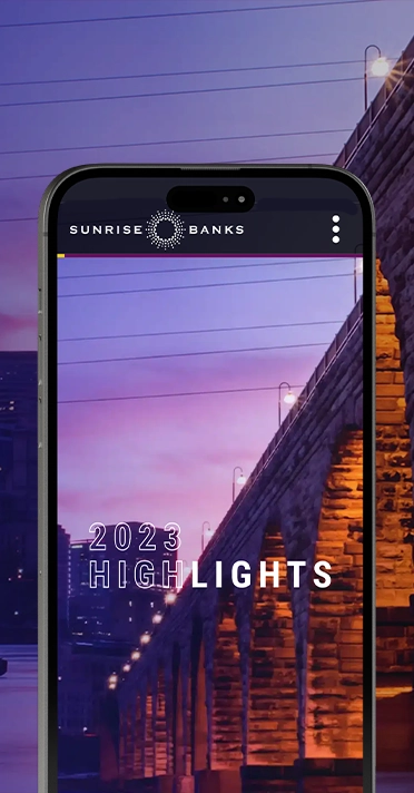 phone screen view of the sunrise banks website against a background of the stone arch bridge in minneapolis